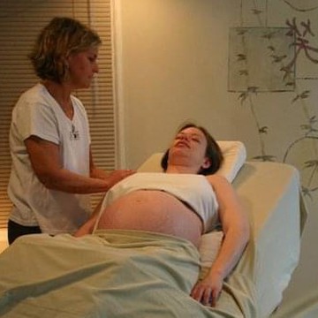 Pregnant woman laying on massage table while receiving a shoulder massage