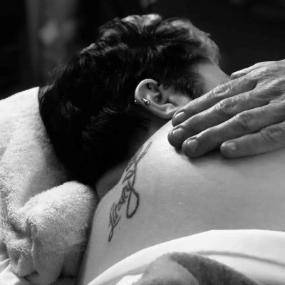 Black and white photo of woman with tattoo on her side receiving a shoulder massage